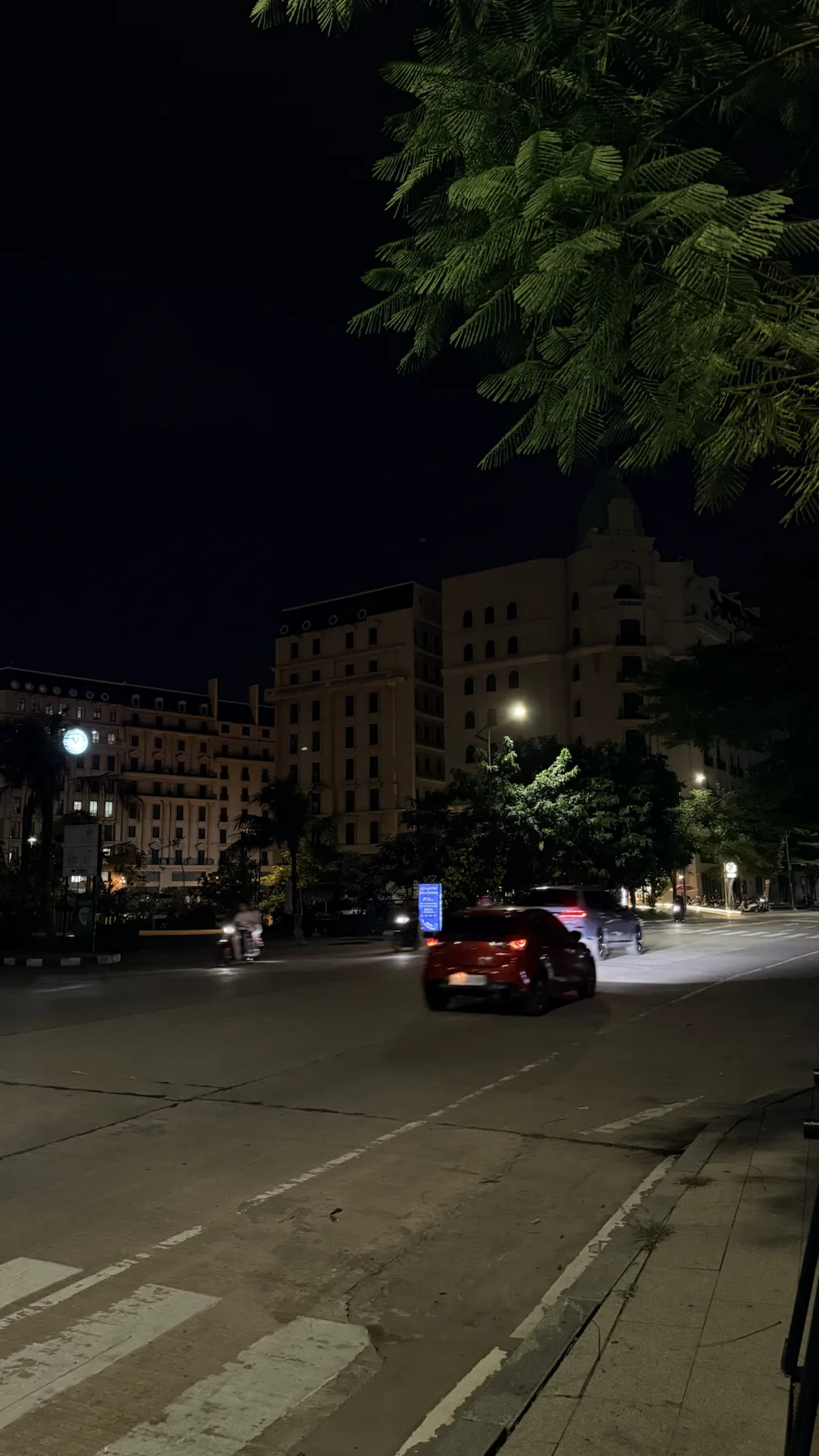 Освещённая улица с автомобилем, деревьями и зданиями в темноте