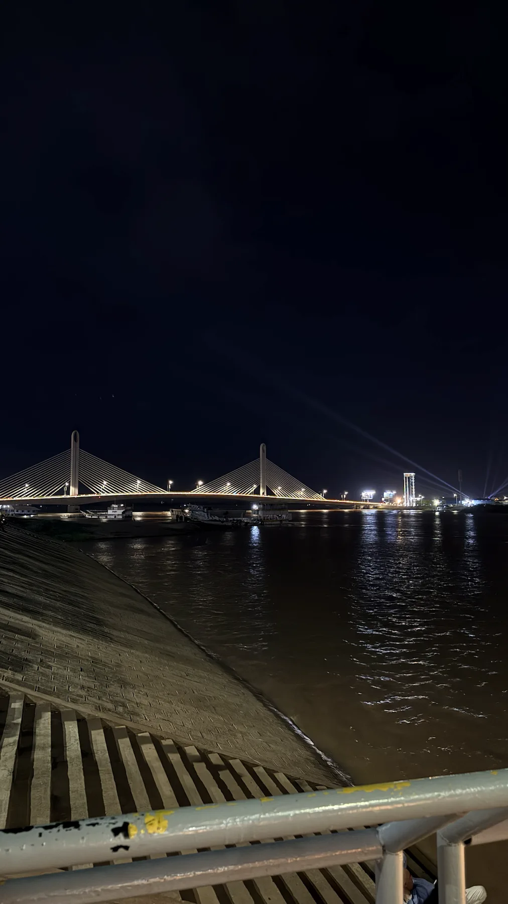 Мост и отражения на воде Подсвеченный вантовый мост над рекой, вид с набережной ночью